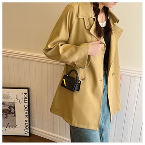 Mini black crossbody bag with grainy texture and gold chain on a khaki blazer model