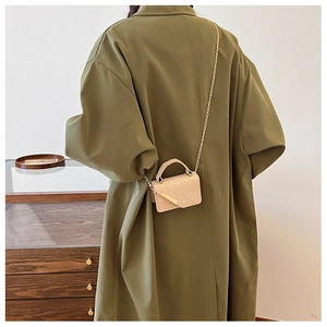 Detail of a mini beige straw bag with gold chain and top handle on green coat