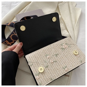 Détail d'un sac bandoulière en paille avec broderie florale et boucle magnétique en métal