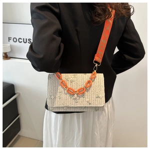 Petit sac en paille brodé de fleurs avec chaîne en acrylique orange porté par un mannequin