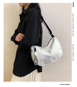 White crescent underarm bag with black adjustable strap and circular charm on model