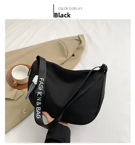 Detail of black nylon crescent shoulder bag with branded webbing strap on white fabric