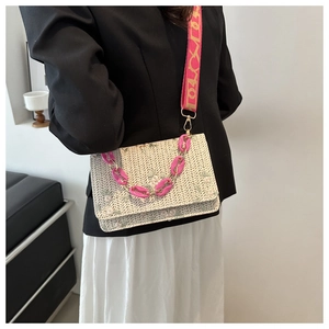 Détail d'un sac bandoulière en paille tissée avec chaîne en acrylique rose et large sangle