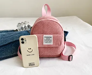 Pink corduroy mini backpack detail showing compact size compared to a smartphone