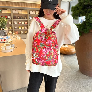 Detail of red floral backpack with peony pattern worn by model in casual setting