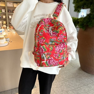 Detailed view of red ethnic floral backpack with pink peony patterns on a model's back
