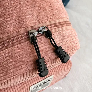 Detail view of the smooth dual zipper on a pink corduroy backpack with textured pulls