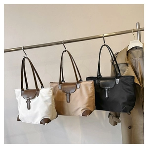 Three large tote bags in white brown and black hanging on a metal rack with a beige trench coat