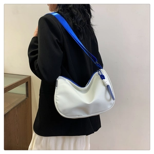 Side view of white half-moon shoulder bag with vibrant blue nylon strap and woven charm