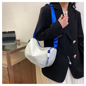 Detail of white nylon crossbody bag with bright blue wide strap and woven pendant