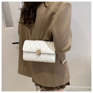 Detail van witte gewatteerde crossbodytas met gouden ketting en ronde sluiting op een model