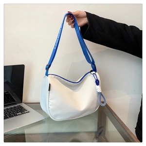 Detail of blue fashion strap and woven knot charm on a white nylon shoulder bag
