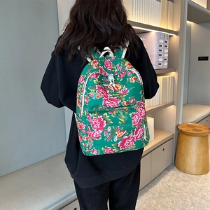 Detail of green canvas backpack with floral peony print shown on a model in a cozy library