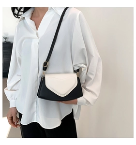 Détail d'un sac bandoulière avec rabat cœur blanc et corps noir porté par un mannequin