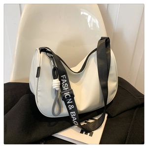 Detail view of white half-moon crossbody bag with branded nylon strap and woven pendant