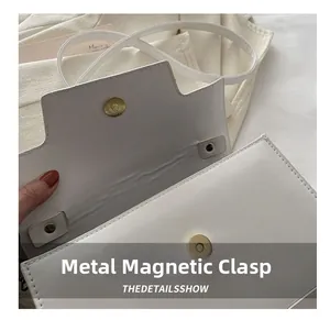 Detail view of the polished golden magnetic snap on a minimalist white leather handbag