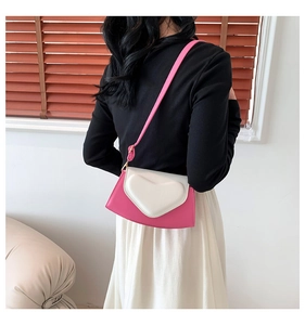 Sac bandoulière rose et blanc avec cœur, porté par un mannequin dans une pièce épurée