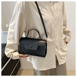 Close-up of a retro black square handbag with a round buckle detail and matte leather finish