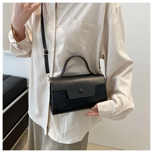 Close-up of a black leather flap handbag featuring a top handle and adjustable strap