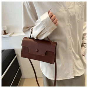 Brown leather crossbody bag shown in a stylish indoor setting with a minimalist vibe