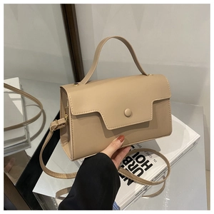 Detail of a beige minimalist handbag held over a book with golden hardware and strap