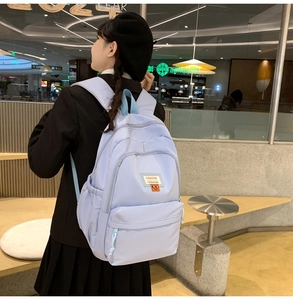 Dettaglio dello zaino in nylon azzurro con etichetta fashion ed emoji arancione