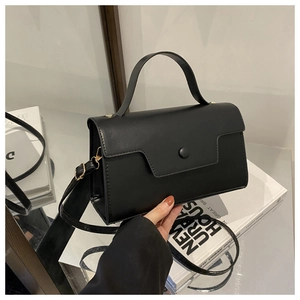 Structured black matte crossbody bag with top handle and round buckle on mirror surface