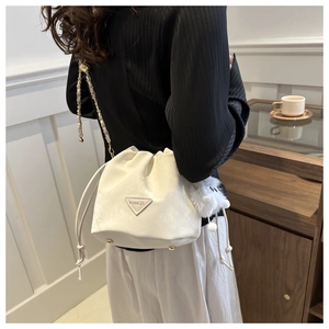 Détail du sac seau en daim blanc cassé avec bandoulière chaîne et pompon en peluche