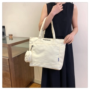Detailed macro view of white canvas tote bag featuring a black FASHION print and mini pouch