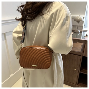 Brown quilted crossbody bag with wide geometric strap and gold metal detail in a home setting