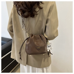 Détail d'un sac seau en cuir marron foncé avec cordon et breloque monstre en peluche