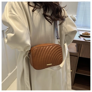 Brown crossbody bag with wave stitching and ethnic woven strap shown on beige coat