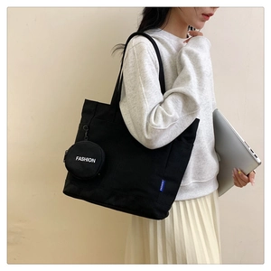 Detail of black canvas tote bag with small zipper pouch shown in a daily commute setting