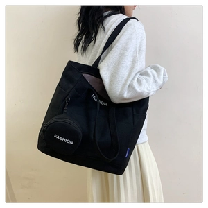 Black canvas tote bag showing side width and decorative blue tag with a round mini pouch