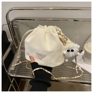 Détail d'un sac seau crème avec bandoulière chaîne et breloque monstre en peluche