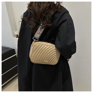 Beige quilted crossbody bag with stylish wide patterned shoulder strap worn by model