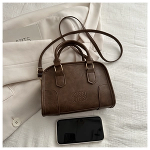 Close-up of textured dark brown Boston bag with embossed logo and golden hardware