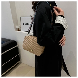 Detail of khaki quilted leather crossbody bag featuring a wide floral embroidered strap
