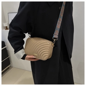 Detail of beige quilted camera bag with stylish wide colorful geometric strap on model
