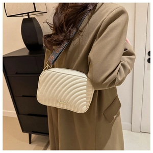 Detail of a beige quilted crossbody bag with wave texture and vintage ethnic pattern strap