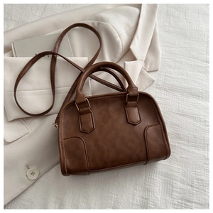 Detailed close-up of dark brown lychee textured handbag with gold hardware on white fabric