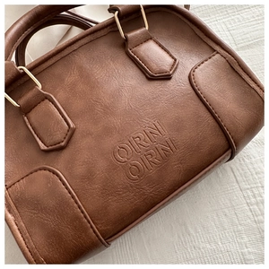 Close-up of brown faux leather texture with ORNI ORNI logo and vintage gold hardware