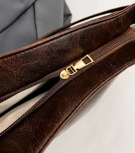 Détail de la texture cuir marron vintage et fermeture éclair en métal doré sur le sac