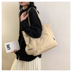 Detail of beige canvas tote bag side profile featuring blue label and round coin pouch