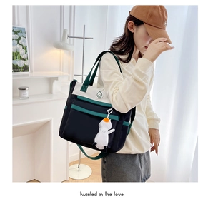Detail of canvas tote bag with contrast green straps, smiley logo, and penguin charm