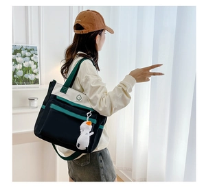 Rear view of a tricolor canvas shoulder bag with a cute white duck plush keychain charm