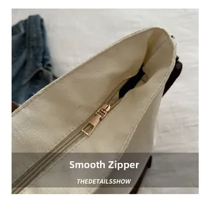 Détail de la fermeture éclair en métal doré lisse sur un sac cabas en toile blanche robuste