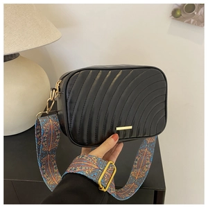 Detail of black quilted wave bag with ethnic geometric wide shoulder strap and gold hardware