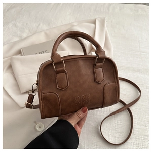 Close-up of brown leather Boston bag with QIRN QIRN logo and vintage gold hardware