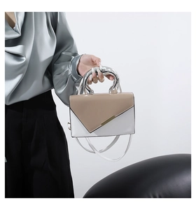 Detail of minimalist bicolored handbag with unique silver fluid metal handle and gold trim